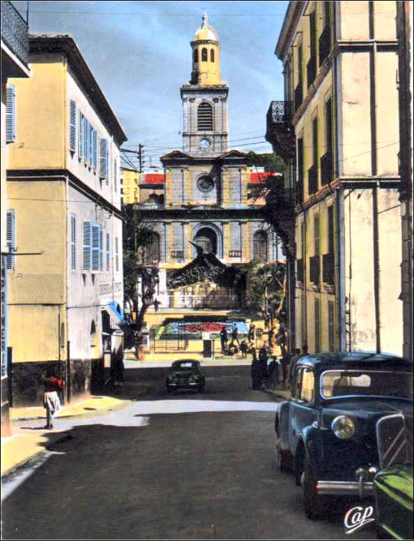 Philippeville - Vue de la Rue Gambetta, l'Eglise et le Monument aux Morts Square Carnot
